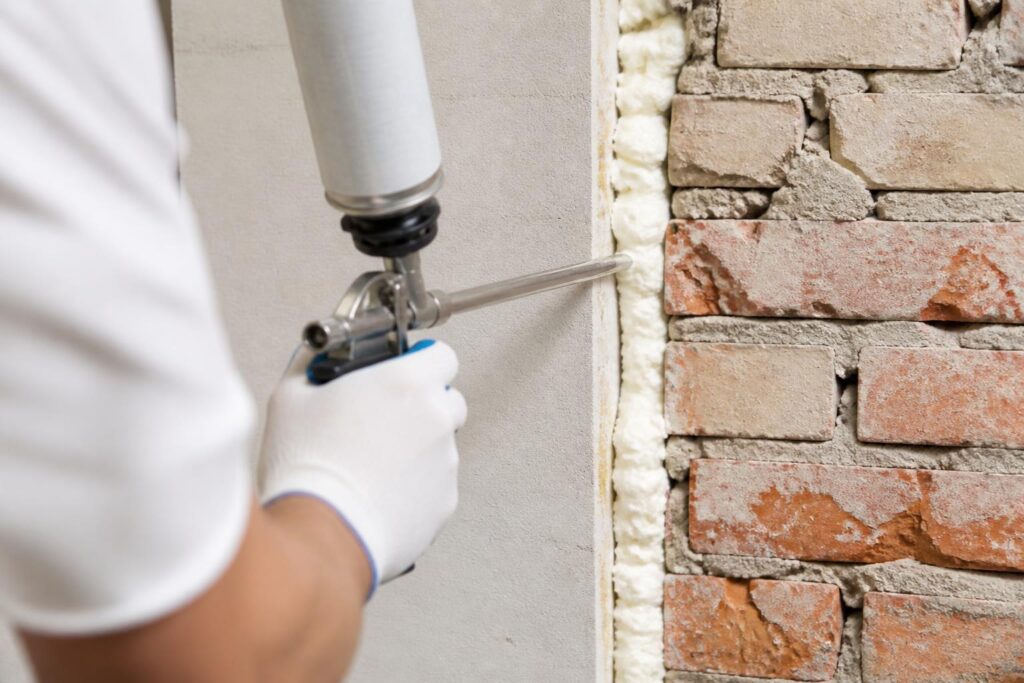 Application de mousse expansive polyuréthane dans un interstice de mur lors de travaux de rénovation.