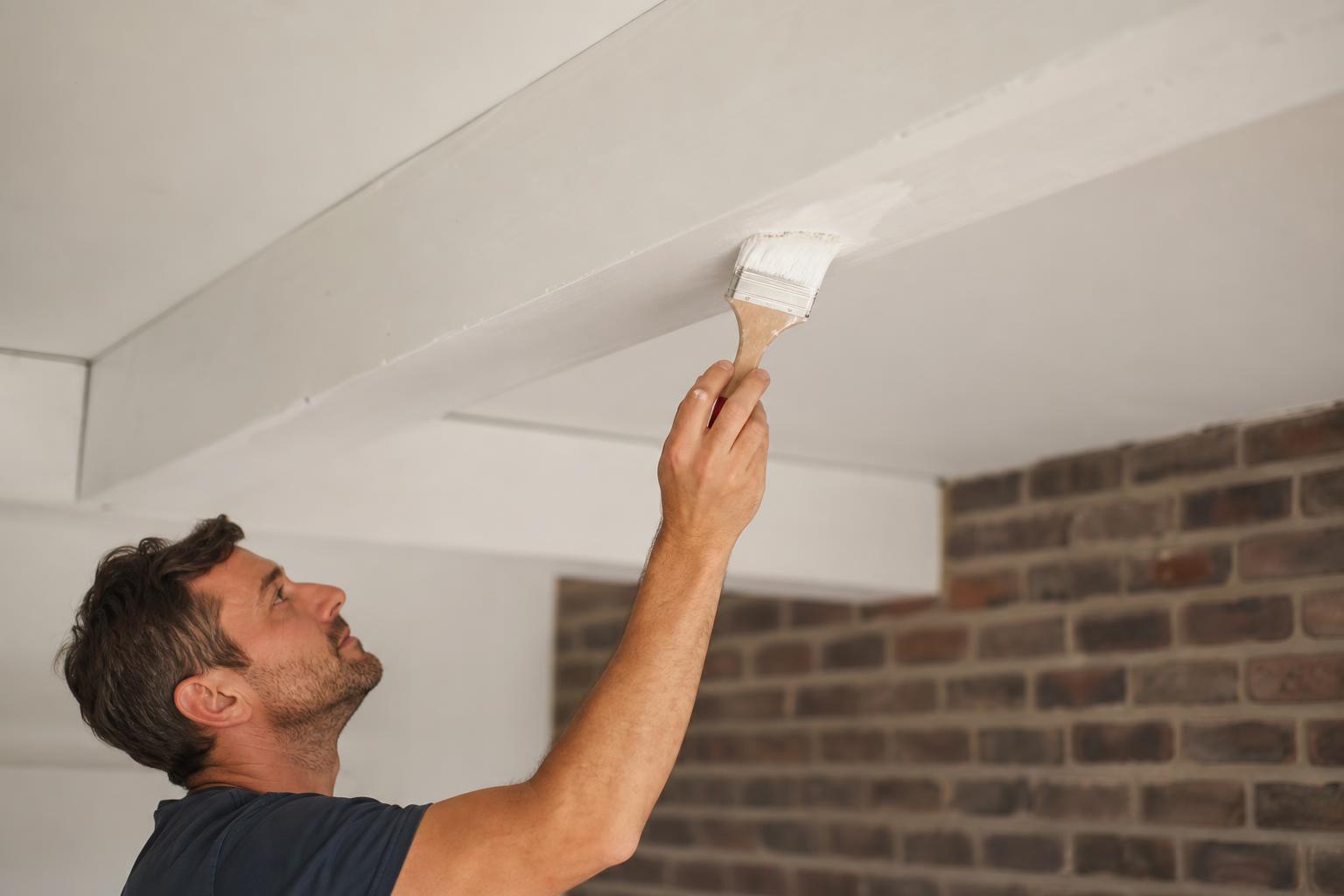 Application de peinture blanche sur une poutre au plafond, au pinceau