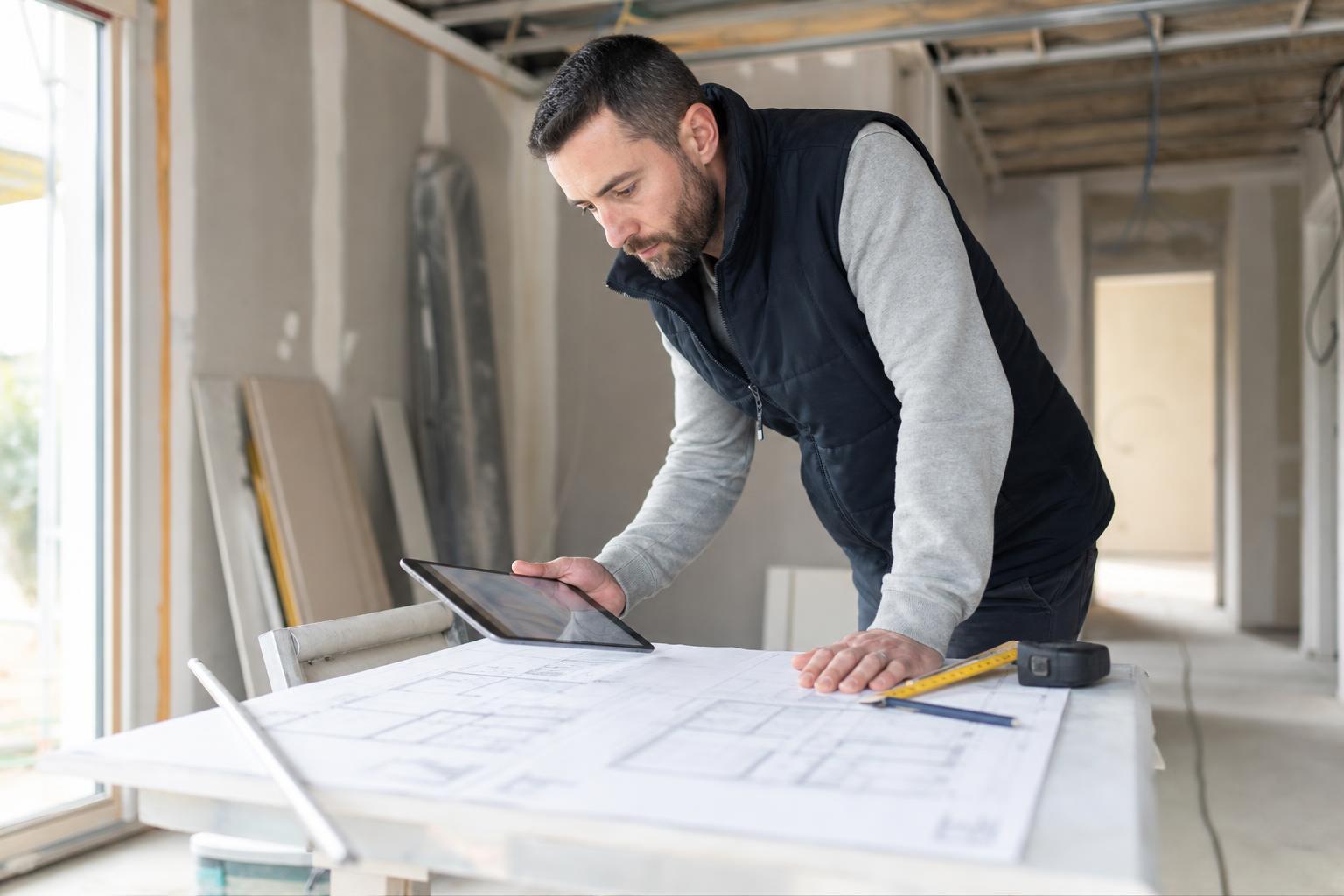 Artisan consultant des plans et une tablette sur un chantier de rénovation