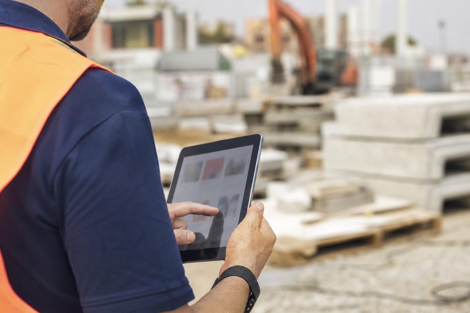Personne consultant un annuaire de fournisseurs de matériaux sur une tablette, sur un chantier