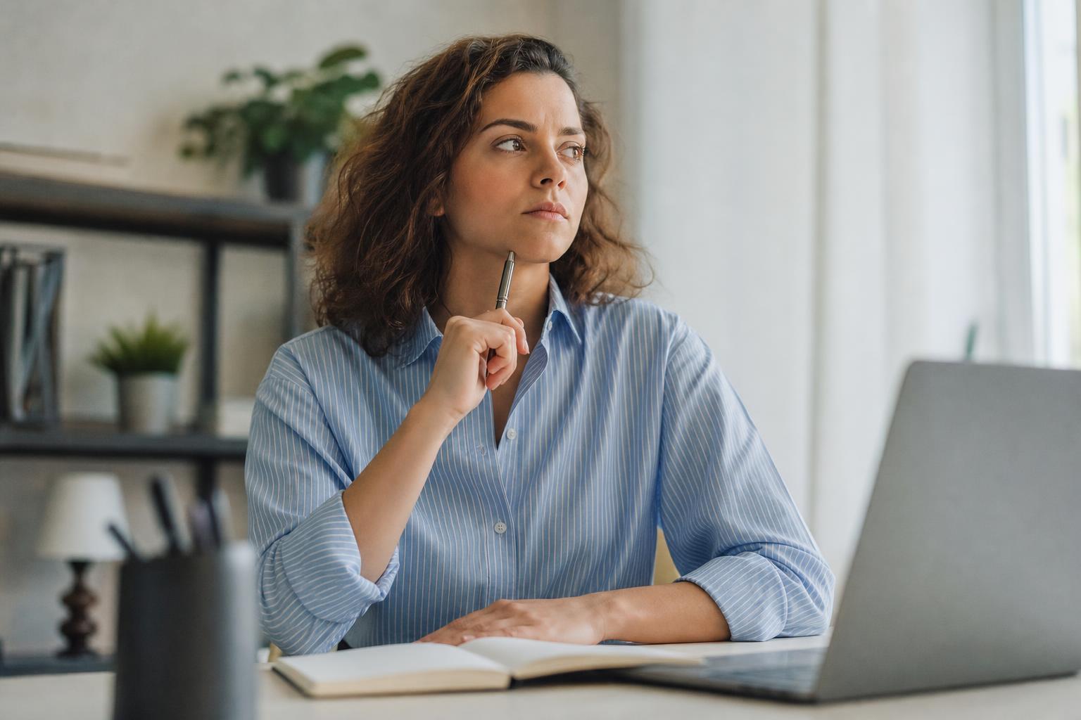 Personne pesant le pour et le contre à un bureau avec un carnet et un ordinateur portable