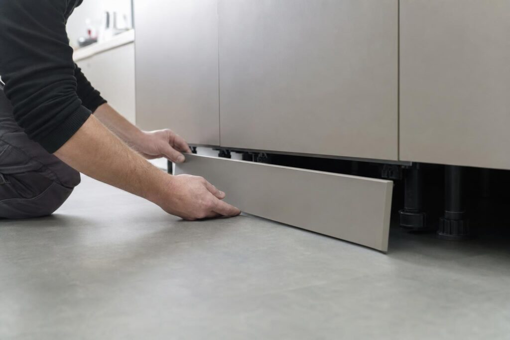 Pose de la plinthe basse des meubles de cuisine, clipsée sur les pieds réglables.