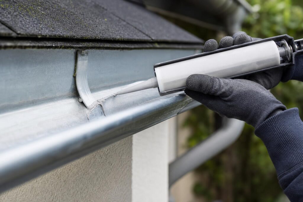 Réparation d'une fuite sur une gouttière en zinc avec du mastic d'étanchéité, sans soudure.
