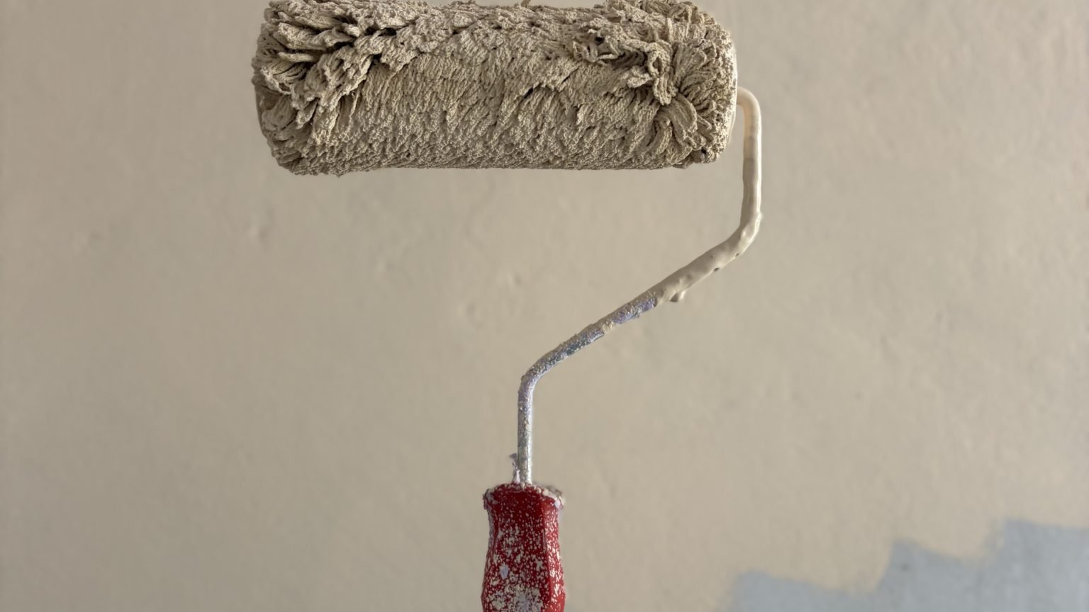 Rouleau de peinture beige tenu contre un mur à moitié repeint